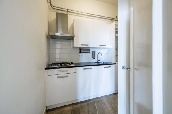 Moderne, compacte witte keuken aan de De Ruijterkade met gaskookplaat, afzuigkap en houten vloer.